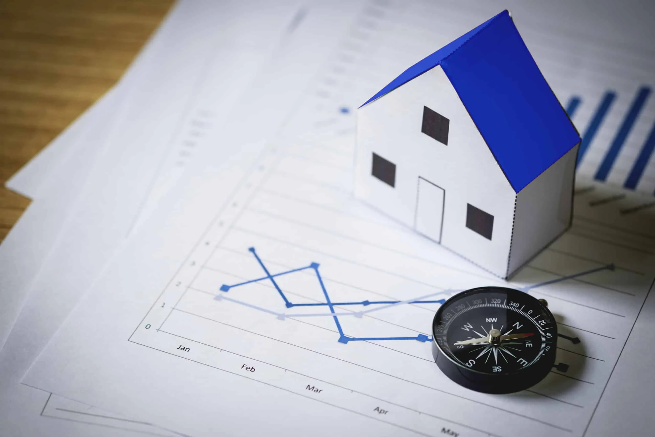 A model house beside a compass and rolled building plans on a desk, symbolising property investment planning