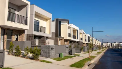 A quiet street of new two-storey townhouses with small front gardens, empty of both cars and buyers