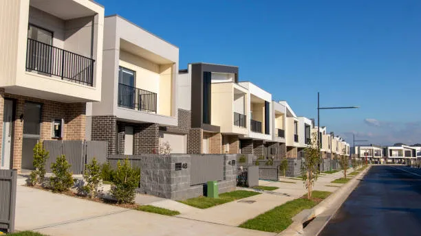 A quiet street of new two-storey townhouses with small front gardens, empty of both cars and buyers