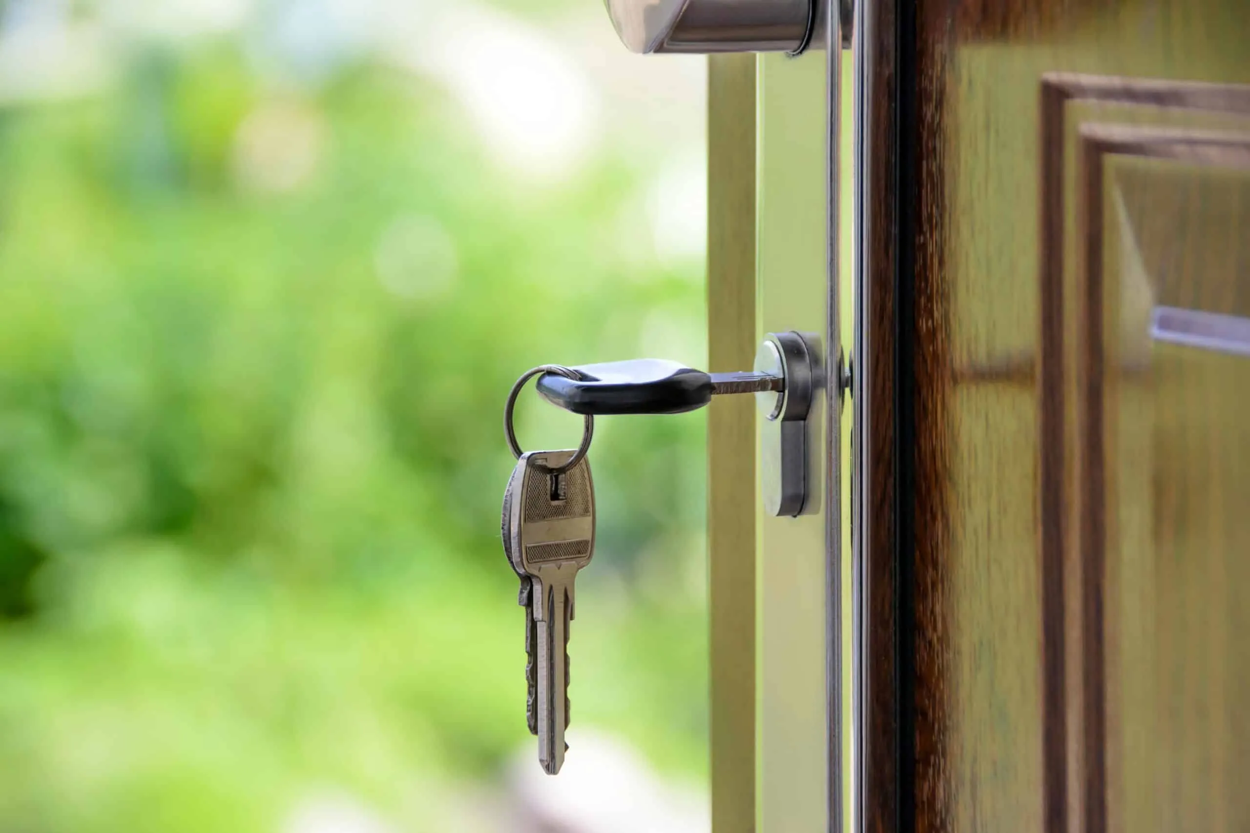 House keys hanging from the lock of a glass front door, garden blurred behind